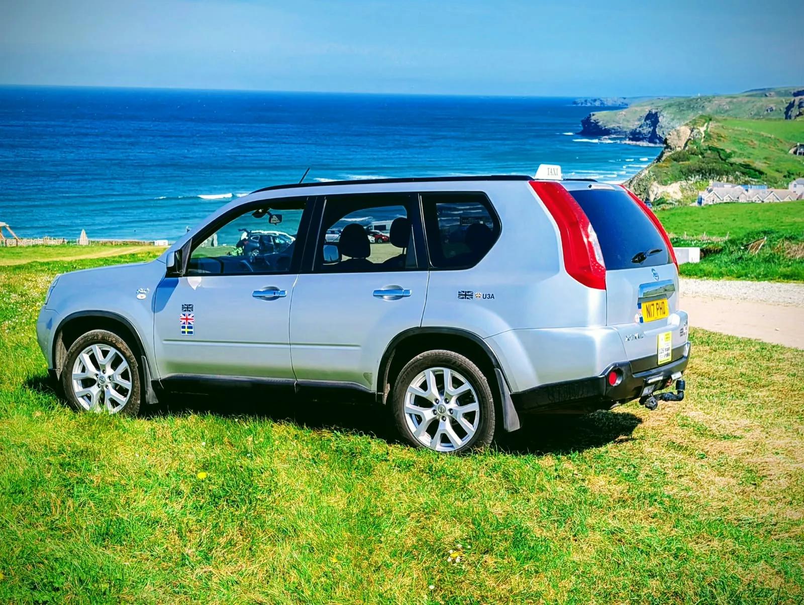 PHD Taxi Services' silver Nissan X-Trail on the clifftop above a Cornish surf beach
